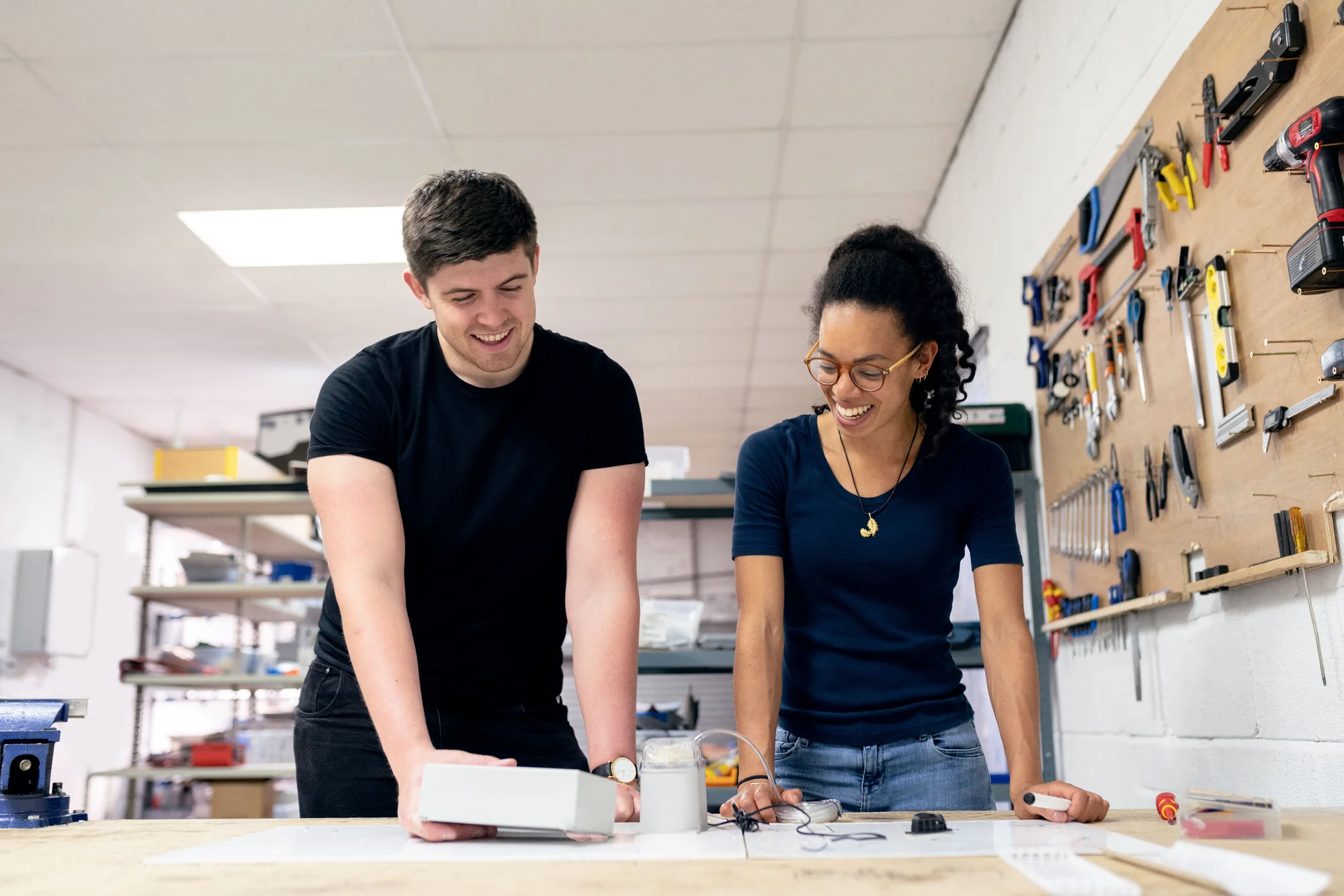 Two people collaborate over a physical prototype at a workshop bench